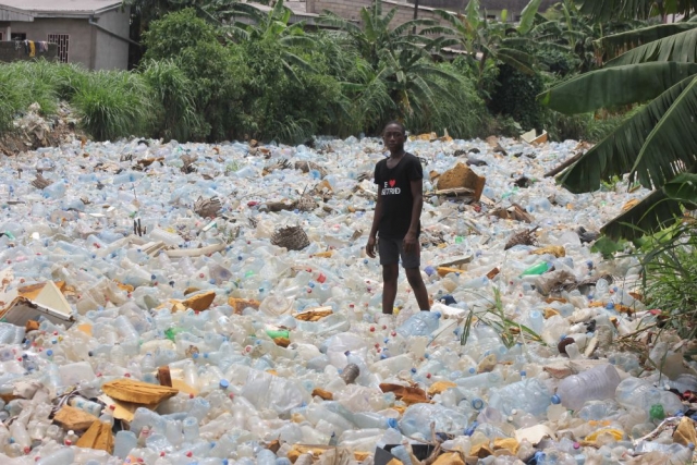 A young man stands in a river of plastic, Douala, Cameroon